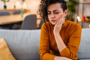 A woman sitting on couch sad with tooth pain in Atlanta, GA 